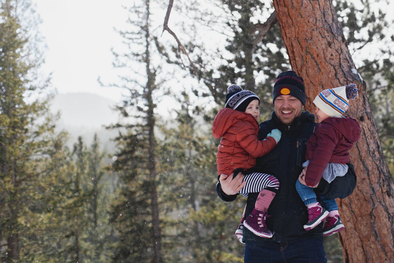 services-04 A joyful father holding his children in a snowy forest during winter, creating lasting memories.