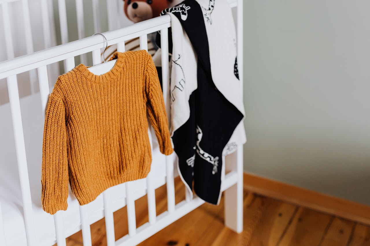services-03 Warm mustard knitted baby sweater hanging on a white crib in an inviting nursery setting.