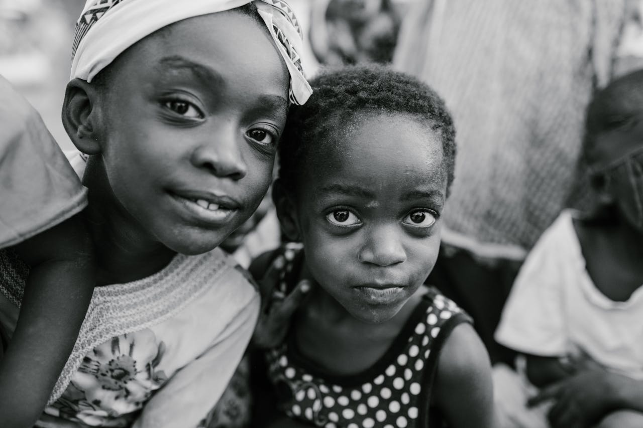 services-02 Black and white glad children in casual clothes standing on authentic town street and looking at camera with curiosity